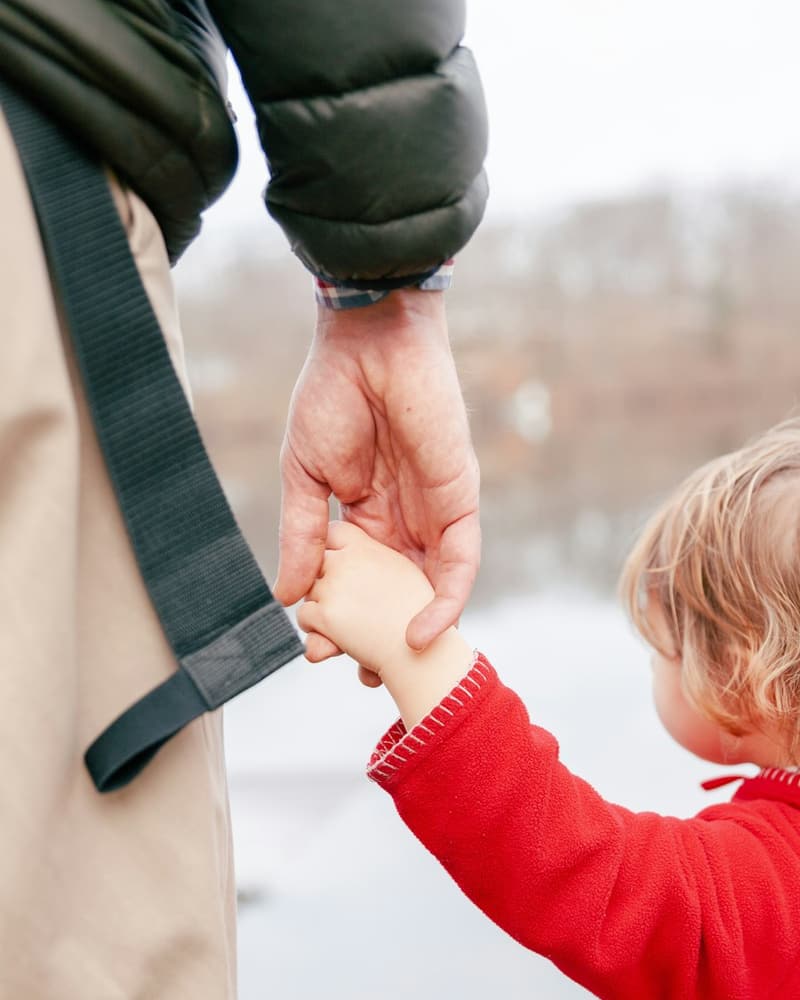 A dad holding his toddler's hand on a walk by the water