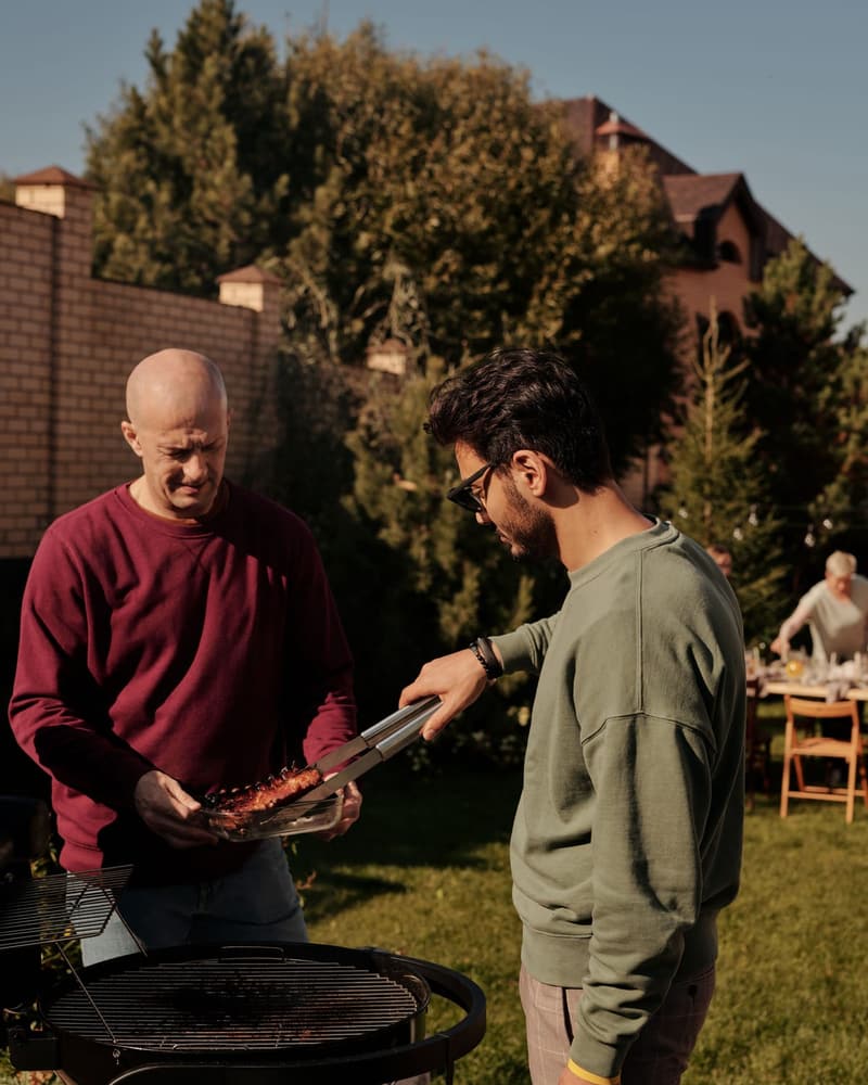 Two dads talking at a backyard grill in late afternoon light